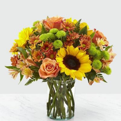 Say hello to autumn with this bouquet filled with bold harvest hues and luscious blooms. Thoughtfully arranged with the freshness of fall in mind, a collection of orange roses, bright sunflowers and orange alstroemeria is set beautifully in a clear glass vase. Whether it's seasonal décor for your home or a gift for a loved one, our Autumn Magnificence Bouquet is sure to make any home its placed in feel warm and bright.